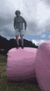 a person is jumping on top of a pink bale of hay .