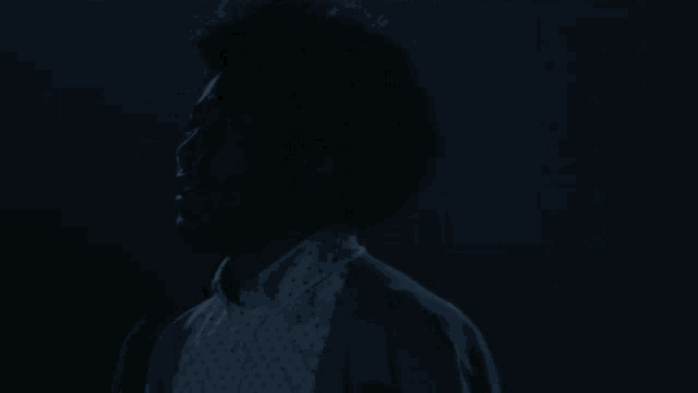a woman with an afro stands in the dark with her eyes closed