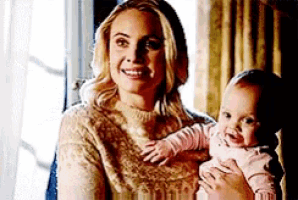 a woman is holding a baby in her arms and smiling while sitting in front of a window .