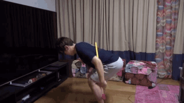 a man is squatting down in a living room with a yellow stick