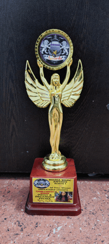 a gold statue of a woman with wings holds a medallion that says ' marina music awards ' on it