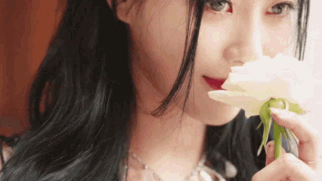 a close up of a woman holding a white flower in front of her face