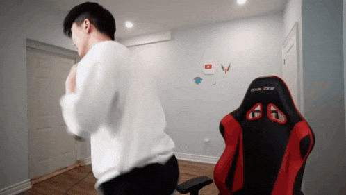 a man in a white shirt is standing in front of a red and black dxracer chair