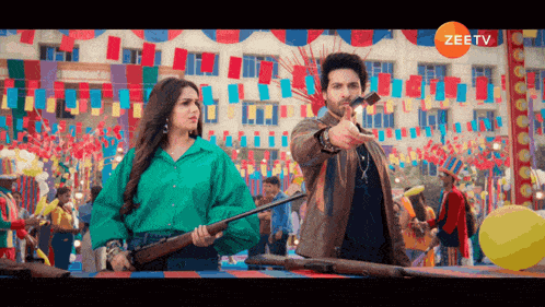 a man is pointing at a woman holding a gun in front of a building that says zeetv on it