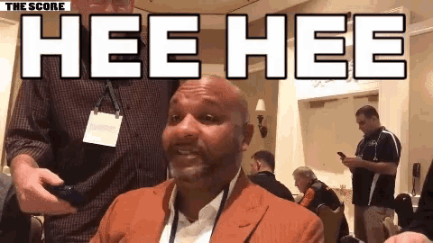 a man in a suit is sitting in a room with the words hee hee written above him .
