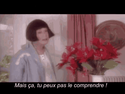 a woman in a blue jacket is standing next to a vase of red flowers in a living room .