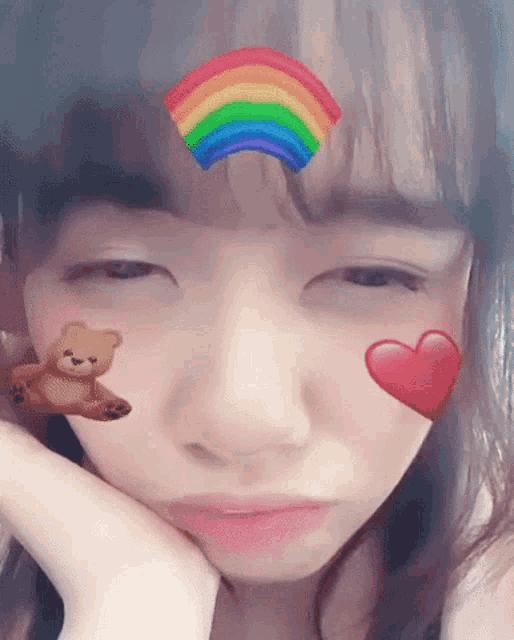 a girl with a rainbow on her forehead and a teddy bear and heart on her face