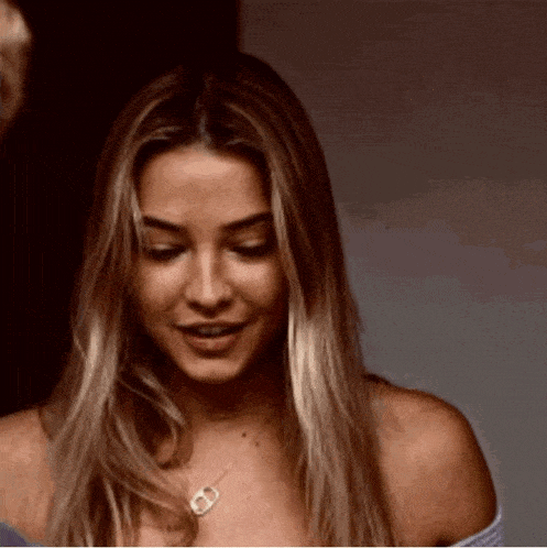 a woman with long blonde hair is smiling and wearing a necklace with the letter d on it .