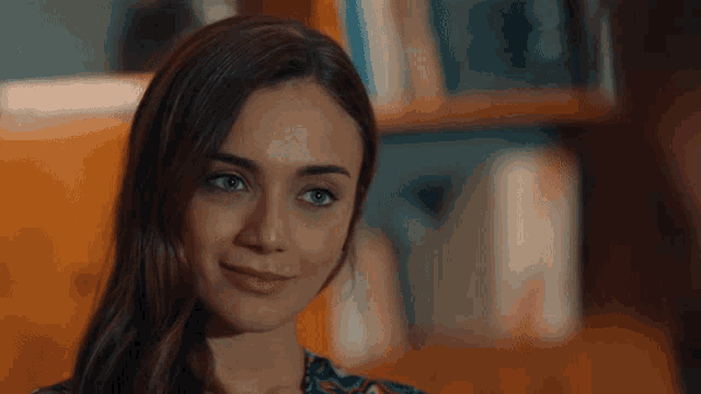 a close up of a woman 's face with a bookshelf behind her