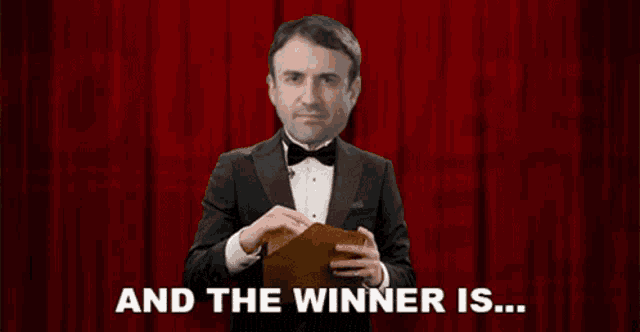 a man in a tuxedo is holding a piece of paper with the words " and the winner is " written below him
