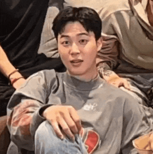a young man in a gray sweater is sitting on a couch with his hands on his knees .
