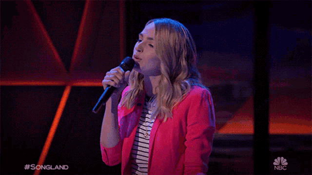 a woman in a pink jacket sings into a microphone on nbc show songland