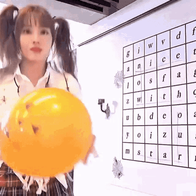 a woman is holding a large orange balloon in front of a word search on a wall .