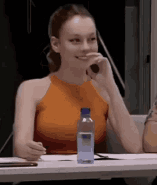 a woman is sitting at a table with a bottle of water and a microphone .