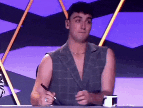 a man in a sleeveless jacket is sitting at a table holding a pen .