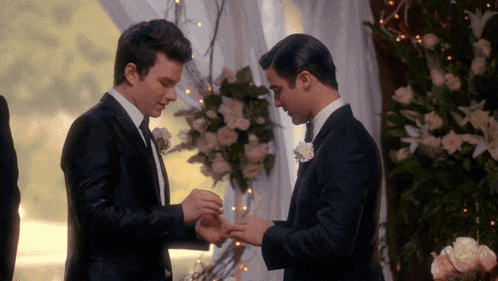 a man putting a ring on another man 's finger at a wedding