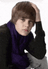 a young man wearing a black sweater and a purple scarf holds his head