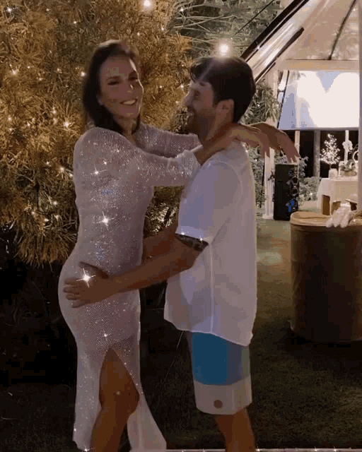 a woman in a white dress is hugging a man in white shorts