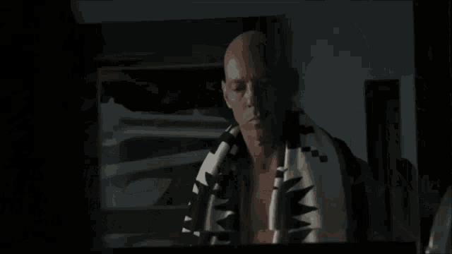 a bald man is wrapped in a black and white blanket with a cross on it