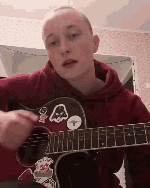 a young man is playing an acoustic guitar with stickers on it