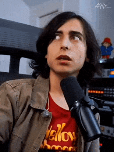 a young man is talking into a microphone while wearing a red t-shirt with the word yellow on it .