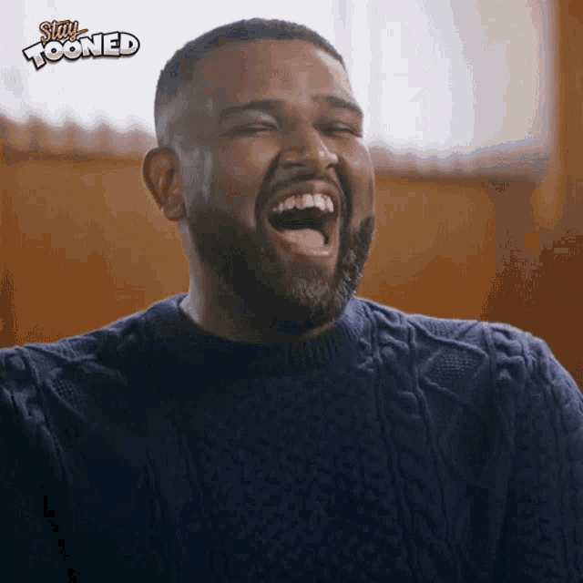a man in a blue sweater is laughing with a stay tooned logo behind him