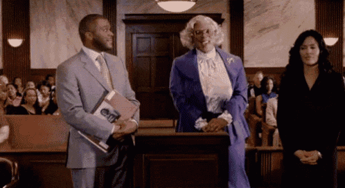 a man in a suit is holding a book while standing next to a woman in a purple dress .
