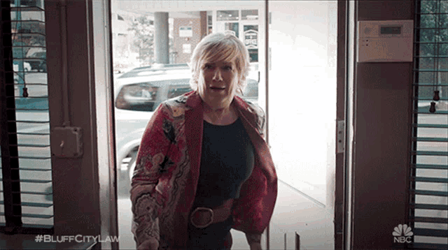 a woman in a red jacket is standing in a doorway with #bluffcitylaw on the bottom