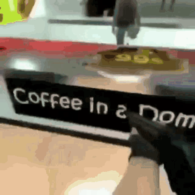 a person pointing at a sign that says " coffee in a nom "