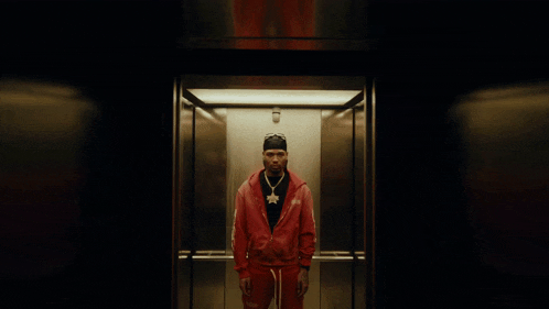 a man in a red jacket is standing in an elevator wearing a beanie and sunglasses