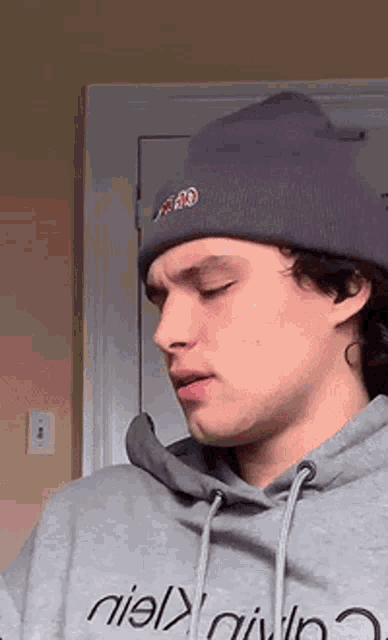 a young man wearing a purple beanie and a grey hoodie is standing in front of a door .