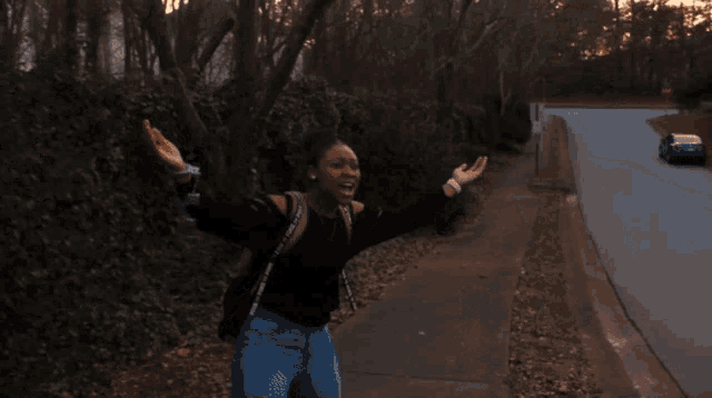 a woman standing on a sidewalk with her arms outstretched wearing a backpack that says victoria 's secret
