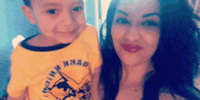 a woman is holding a young boy who is wearing a yellow shirt that says " duck hunt "