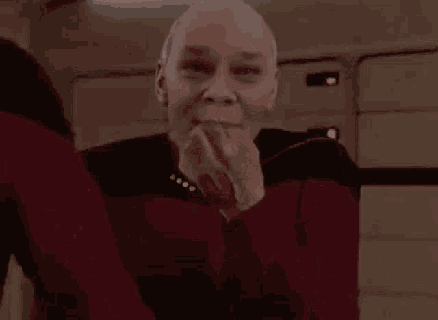 a bald man in a red sweater is covering his face with his hands .