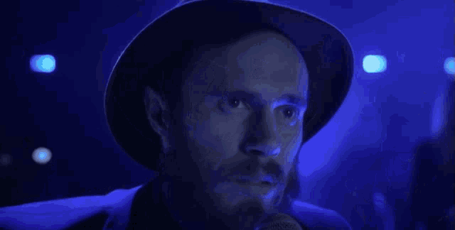 a man with a beard is singing into a microphone while wearing a hat