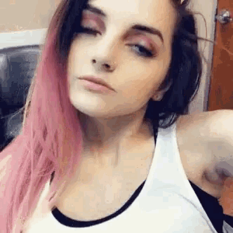 a woman with pink and black hair is taking a selfie .