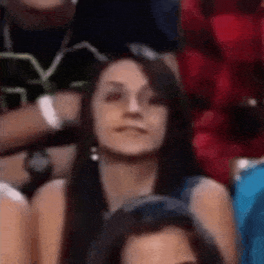 a woman is sitting in a crowd of people and looking at the camera .