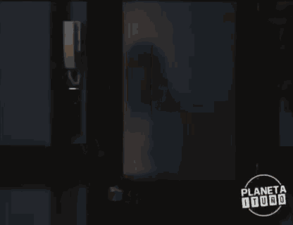 a woman in a white shirt is standing in front of a door with planeta toro written on it
