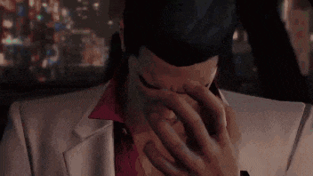 a man in a suit is covering his face with his hands in a car .