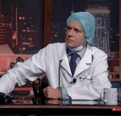 a man in a lab coat and surgical cap sits at a table