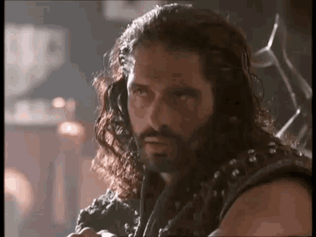 a man with long hair and a beard is standing in a dark room and looking at the camera .