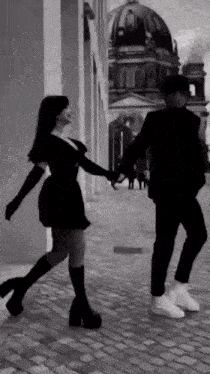 a man and a woman are holding hands while walking down a street .
