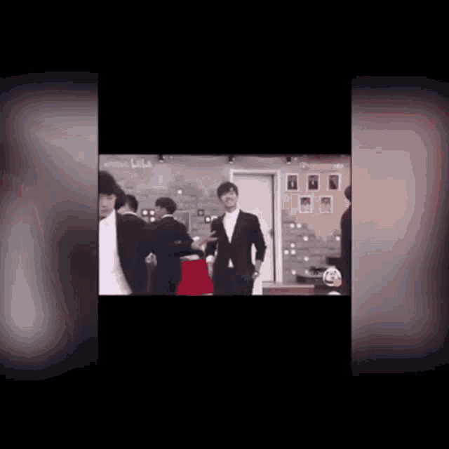 a man in a suit is standing in a room with other people .
