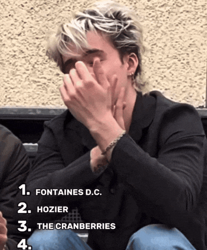 a man covering his face with his hands with the words fontaines d.c. hozier the cranberries and the cranberries next to him