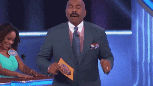 a man in a suit and tie is holding a piece of paper that says family feud ..