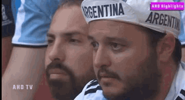 two men wearing argentina hats are watching a soccer game .