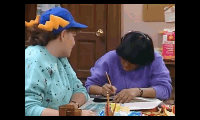 a woman wearing a blue hat is sitting at a table with another woman writing in a notebook