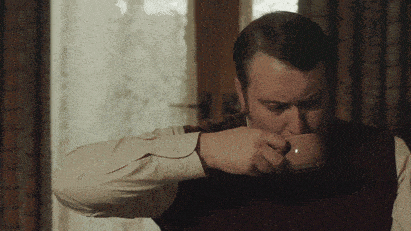 a man in a vest is drinking from a brown mug