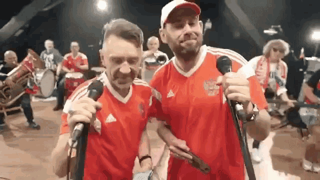 two men singing into microphones while wearing red shirts