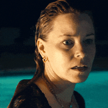 a close up of a woman 's face in front of a pool at night